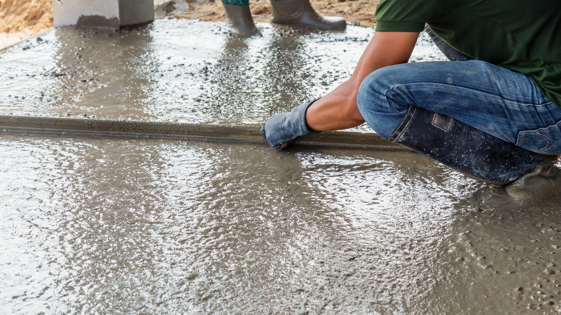 Concrete finisher kneeling to screed a freshly poured concrete slab