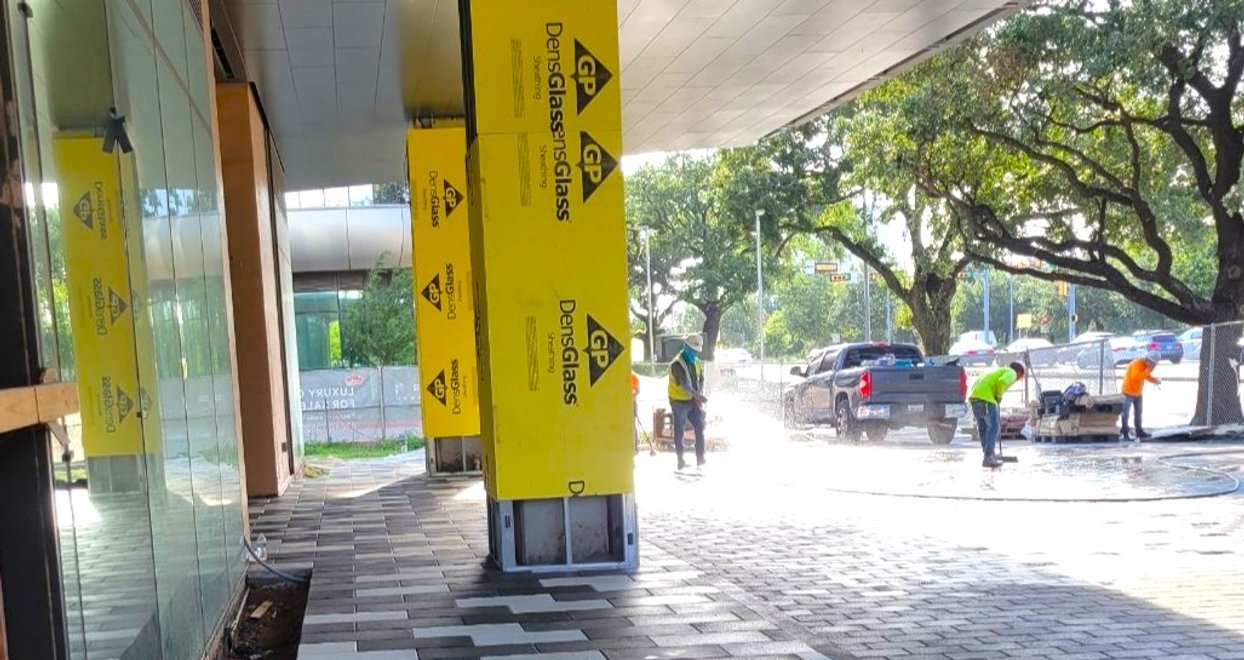 Crew cleaning a new two-tone paver walkway under the canopy of a commercial building