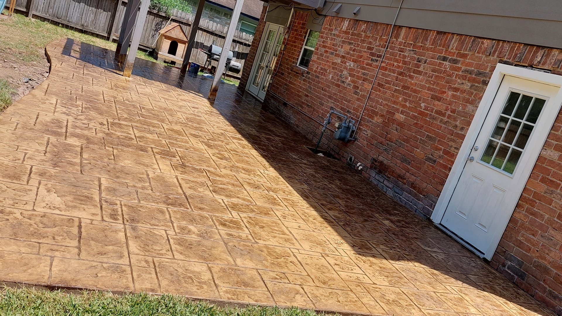 New stamped concrete patio with a tan stone pattern and a curved edge behind a brick home