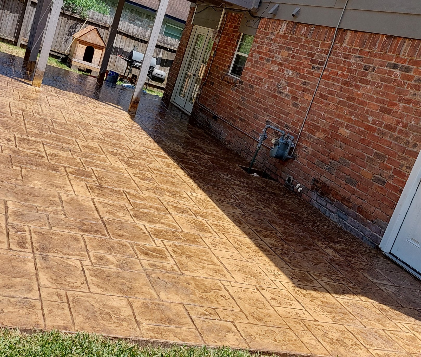 New stamped concrete patio with a tan cut-stone pattern and a curved edge behind a brick home