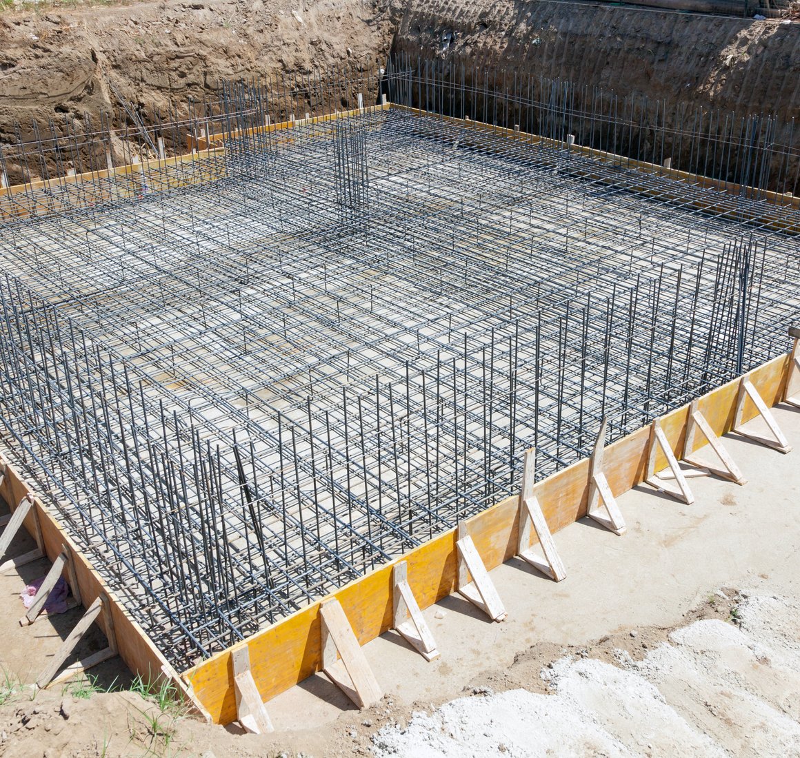 Dense steel rebar grid set inside yellow wood forms before a concrete foundation pour