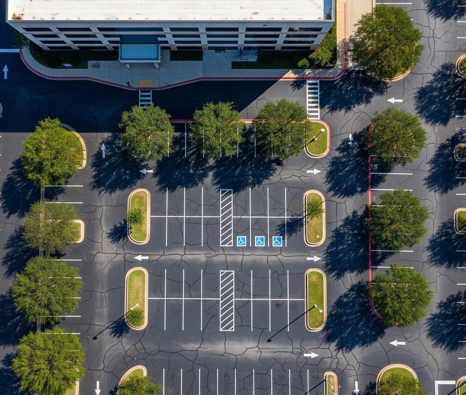 Aerial view of an office parking lot with cracked pavement, striped stalls, and accessible parking spaces